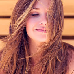 Imagem de uma mulher loira sorrindo com os olhos fechados, feliz por estar com seu cabelo saudável