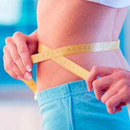 Imagem de uma mulher com foco na cintura dela com uma fita métrica em volta da cintura
