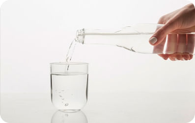 Foto de um copo com uma pessoa enchendo esse copo de água com uma garrafa
